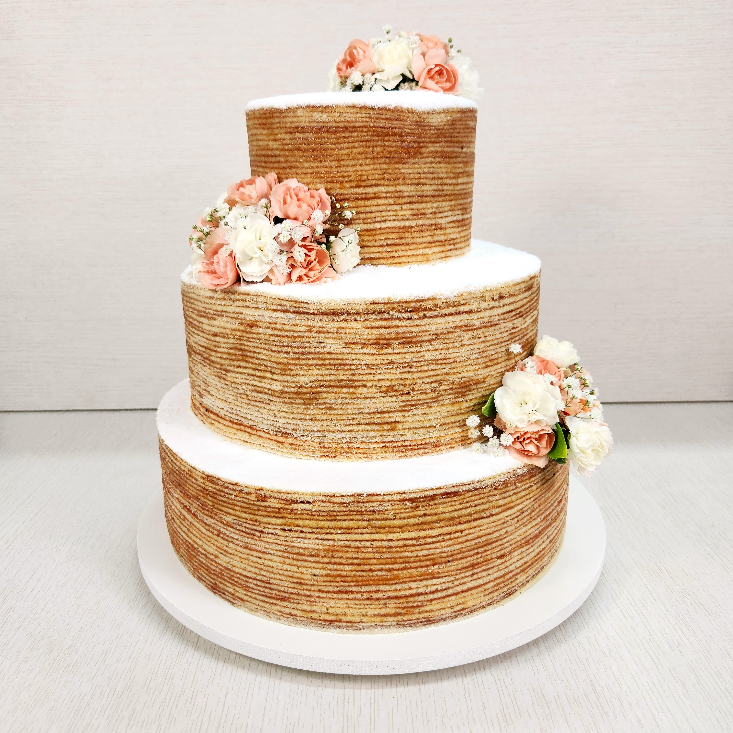 Bolo de casamento de três andares feito com camadas de bolo de rolo, decorado com flores nas cores do casamento, unindo elegância e estilo personalizado.